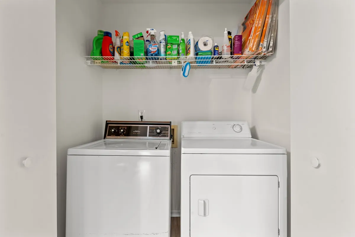 A dedicated laundry closet featuring a washer, dryer, and organized shelves with cleaning supplies. The scene conveys convenience and practicality, emphasizing the added value for families or long-term guests.