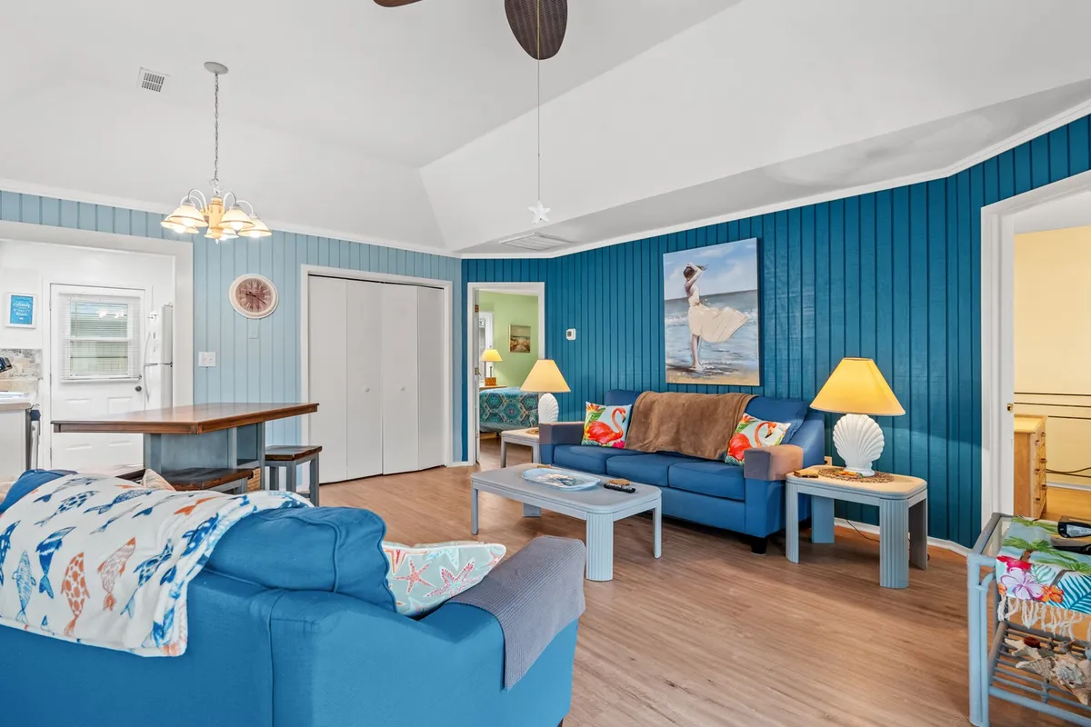 The image showcases a bright, welcoming living room with plush blue sofas accented by colorful cushions, a charming dog artwork on the wall, and a cozy table with lamps—creating an inviting space perfect for gathering with friends and family.
