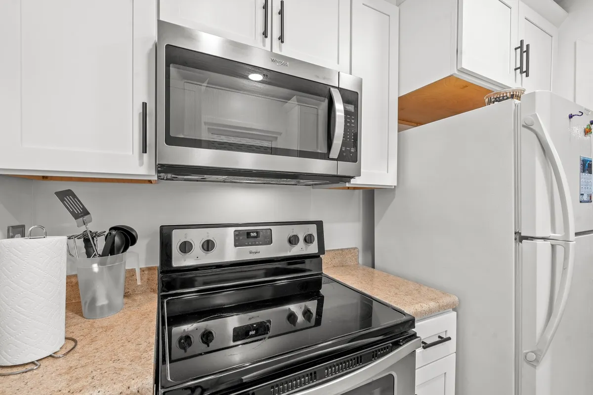 A close-up view of the kitchen area, highlighting a sleek stainless steel microwave, a black stove, white cabinetry, and a granite countertop. The scene emphasizes the kitchen's functionality and up-to-date appliances, inviting guests to prepare their favorite recipes.