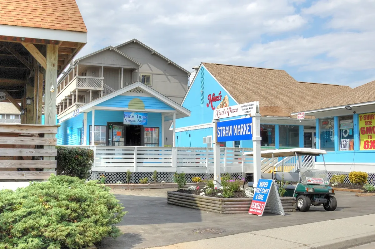 A cheerful exterior streetscape with colorful storefronts, a golf cart parked by the curb, and visible market signs. The scene buzzes with energy, reflecting local commerce and leisure activities.