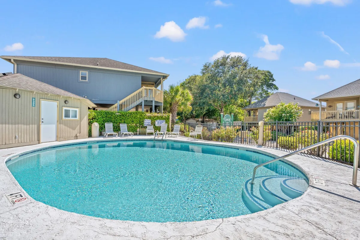 A sparkling swimming pool surrounded by lounge chairs and lush greenery, inviting guests to relax, swim, and socialize in a sun-drenched outdoor setting. The tranquil atmosphere is enhanced by well-maintained landscaping and open skies, suggesting resort-style amenities and a communal vibe.