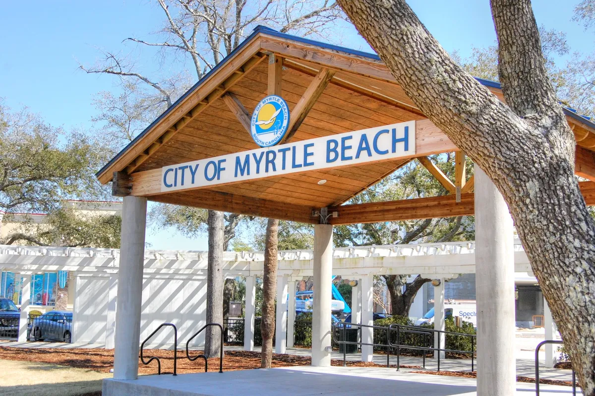 This image features the City of Myrtle Beach sign set within a welcoming wooden pavilion structure, surrounded by trees. The scene is open to the community, suggesting a place where gatherings and local events take place.