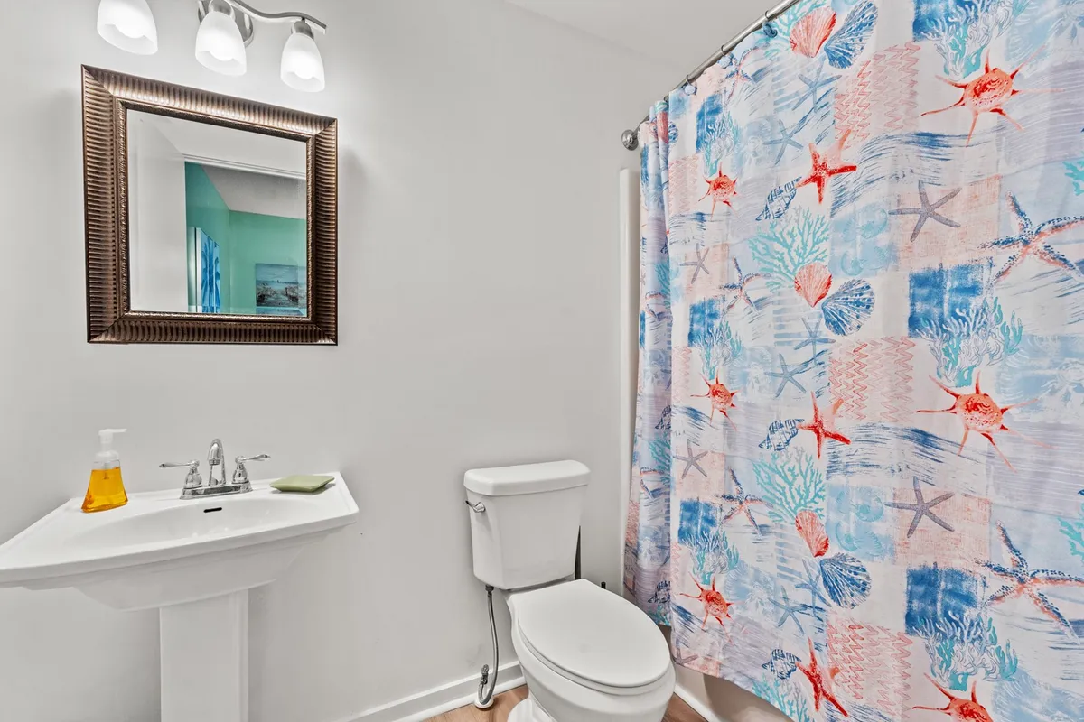 A cheerful, modern bathroom featuring a vibrant shower curtain, a sleek sink with a framed mirror, and clean finishes. The inviting atmosphere makes this a perfect spot to refresh and unwind, evoking a spa-like experience.