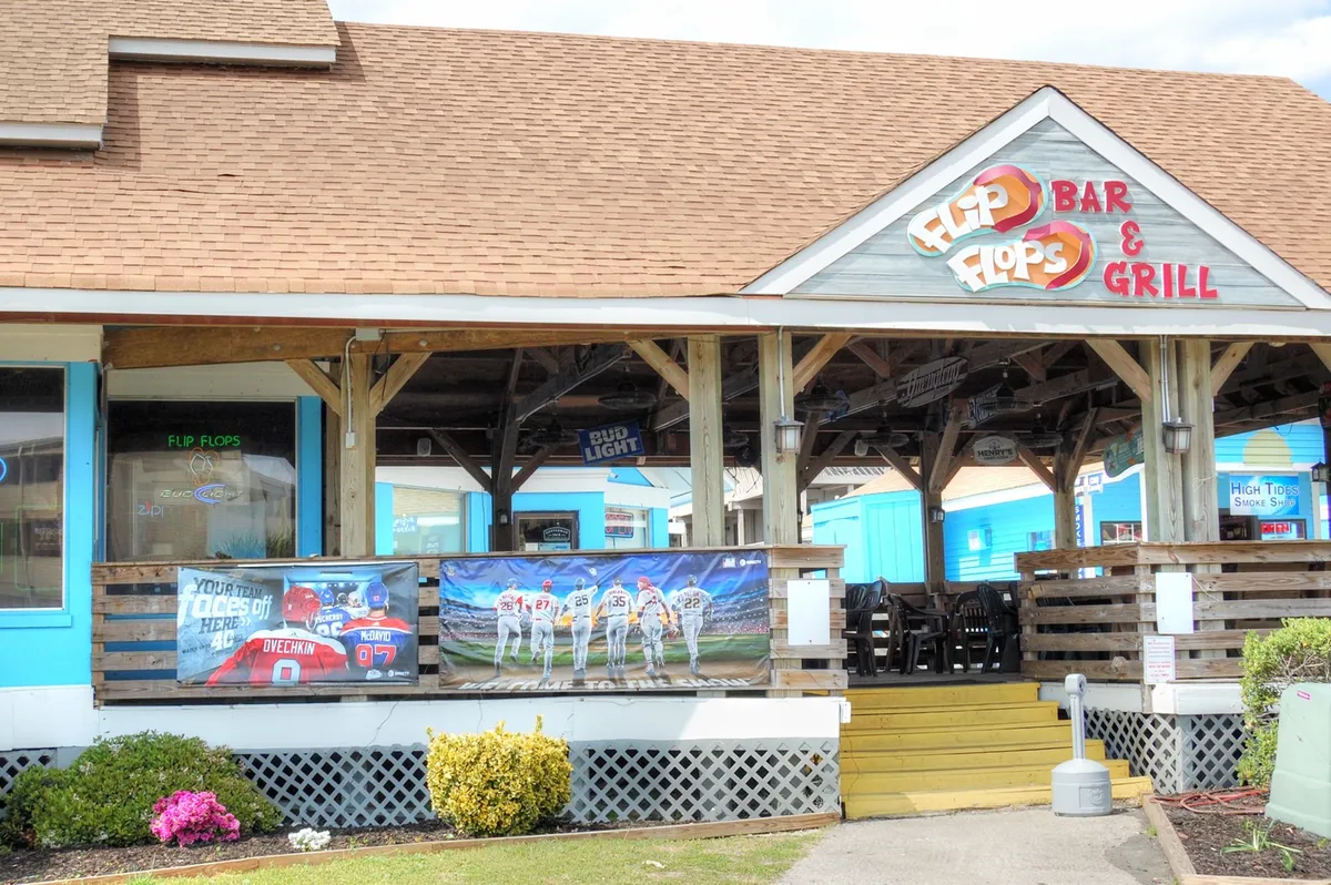 An exterior shot showing the 'Flip Flops Bar & Grill' sign, lively outdoor seating, and vibrant banners. The setting feels casual and inviting, perfect for socializing and experiencing local flavors.