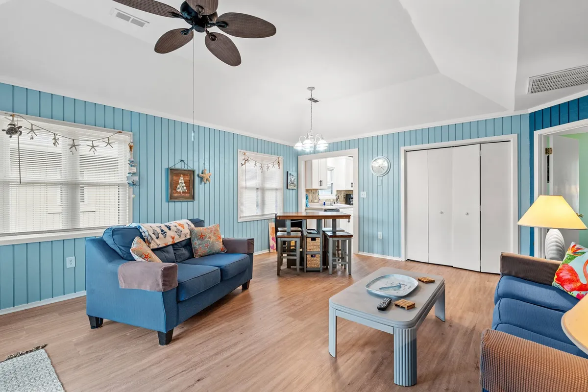 This image features a cozy, open-concept living and dining space. Blue sofas provide comfortable seating while a well-sized dining table is perfectly suited for family meals or game nights. Decorative wall elements add a touch of coastal charm, and natural light streams in, illuminating the entire area.