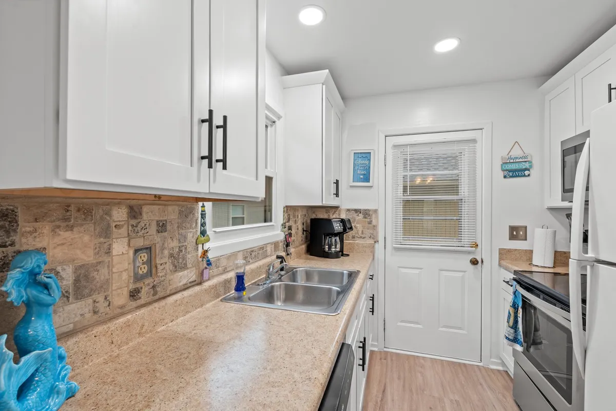 This image showcases the central kitchen space with inviting white cabinetry, modern stainless steel appliances, ample countertops, and a whimsical mermaid statue adding character. The overall scene is bright and functional, emphasizing the kitchen's suitability for group cooking, entertaining, and family gatherings.