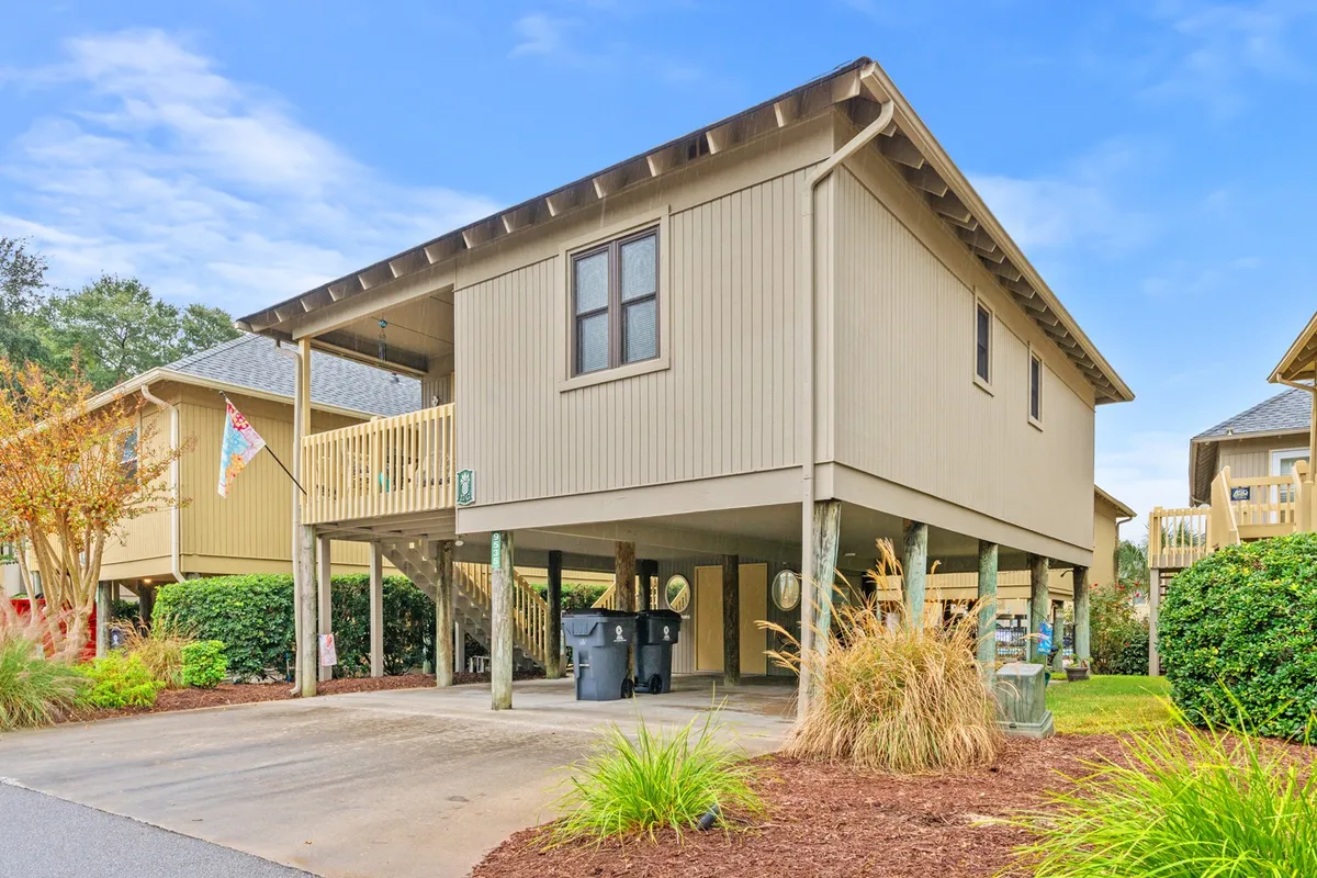 A welcoming exterior view of the house, showcasing the structure, balcony, landscaped driveway, and under-house parking area. The image hints at the convenience and ease of arrival, as well as opportunities for outdoor gatherings and relaxation.